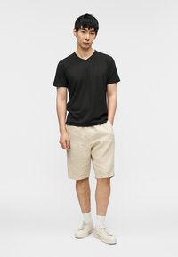 Μαύρο βαμβακερό T-shirt με V-λαιμόκοψη, μπεζ λινό σορτς και λευκά αθλητικά παπούτσια με ανοιχτό γκρι κάλτσες. Απλός σχεδιασμός, άνετη γραμμή, χωρίς σχέδια ή διακοσμήσεις.