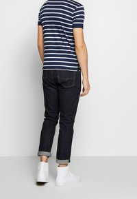 Proužkované námořnické a světle modré tričko s krátkým rukávem, spárované s tmavými džíny, ohrnutými manžetami a bílými vysokými teniskami.