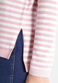 Ljusrosa och vita randiga tröja med ribbad nederkant och sidofickor, kombinerad med mörkblå denim. Texturerna ser mjuka och stickade ut.