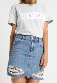 Grå bomulls-T-shirt med vit "TOMMY"-logotyp och en denimkjol med slitna detaljer och fransad nederkant, i ljusblått.