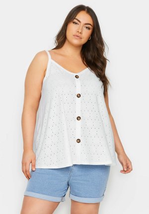 Top blanco sin mangas con cuello en V, tela texturizada con perforaciones y cierre frontal con botones de madera oscura. Combinado con shorts de mezclilla.