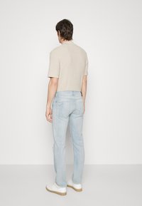 Camisa de manga corta de color beige claro con textura, combinada con jeans azul claro con detalles desgastados. Zapatillas blancas completan el conjunto.