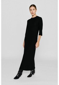 Schwarzes, geripptes Maxikleid mit Dreiviertelärmeln und Rundhalsausschnitt. Der Stoff hat vertikale Streifen und wird mit knöchellangen, glänzenden schwarzen Stiefeln kombiniert.