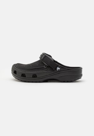 Sabot noir avec une tige texturée, une sangle réglable et des trous de ventilation. Conçu avec une semelle rembourrée et des détails de couture discrets.