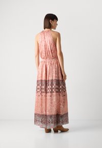 Robe maxi en tissu rose avec des motifs floraux et géométriques. Design à encolure halter, taille élastique, longue jupe fluide, assortie à des bottes marron.