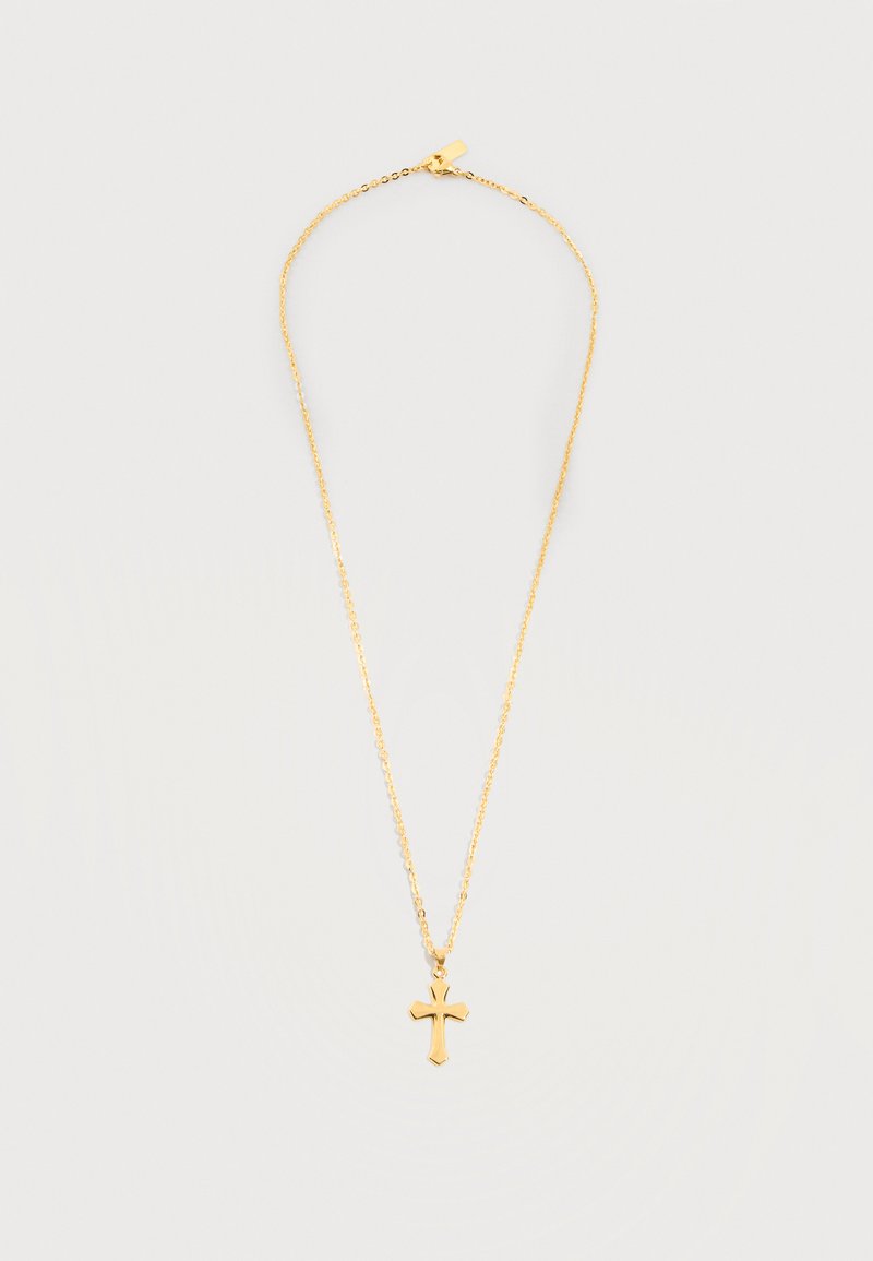 Χρυσό κολιέ με αλυσίδα και μικρό γυαλιστερό σταυρό ως μενταγιόν σε απλό φωτεινό φόντο.