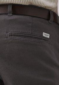 Dunkelgraue Hose mit glatter Textur, ausgestattet mit einer Gesäßtasche mit horizontaler Öffnung und einem kleinen, aufgenähten Markenlabel.