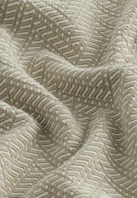 Tissu beige avec motif géométrique en zigzag et points en relief, montrant des plis doux et une surface texturée.