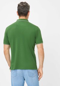 Polo verde con maniche corte, caratterizzato da un colletto e bordo bianco a contrasto alle estremità delle maniche, abbinato a jeans azzurri chiari.