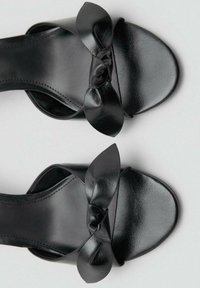 Black leather sandals with a wide strap and a knotted bow detail on the front, featuring a smooth texture and open toe design.