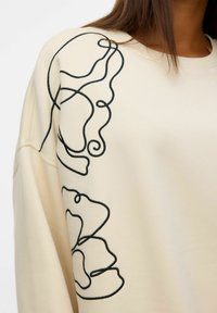 Felpa crema con ricami astratti neri, vestibilità oversize, tessuto morbido e scollatura rotonda.