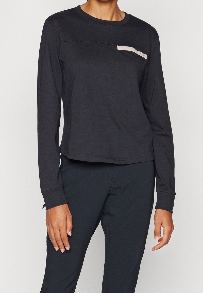 Black long-sleeve shirt featuring a chest pocket with a beige detail. Made of soft fabric with a relaxed fit and stitched hem.