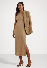 Vestido de punto sin mangas en un tono beige claro con un patrón texturizado. Presenta una abertura lateral y se combina con una blazer texturizada. Sandalias de tacón.