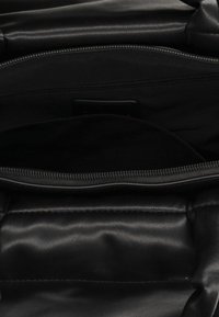 Interiér černé kožené kabelky s jemnou texturou, zipovou kapsou a hladkým povrchem. Obsahuje centrální kapsu s podšívkou.
