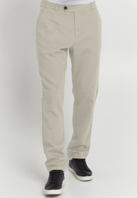 Beige Hose aus Baumwollmischung, mit flachem Bund, Gürtelschlaufen und Seitentaschen. Kombiniert mit schwarzen Sneakers.