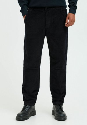 Zwarte corduroy broek met een recht model, voorzien van voorzakken en een knoopsluiting. Gecombineerd met zwarte veterschoenen.