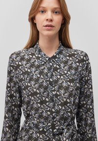 Hemd mit Knöpfen, das einen dunklen Hintergrund mit einem floralen Muster in Blau und Weiß zeigt, lange Ärmel, Kragen und ein gebundenes Taillendetail hat.