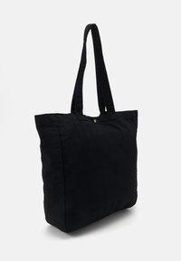 Zwarte katoenen tote bag met twee lange handvatten, rechthoekige vorm, zachte textuur en een enkele messing drukknoopsluiting aan de bovenkant.
