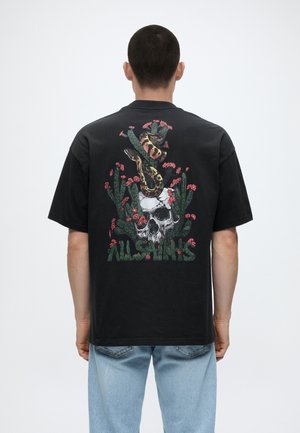 Mand iført sort t-shirt med grafik af en slange snoet omkring en kranium og kaktusser omgivet af lyserøde blomster samt teksten "AllSaints".