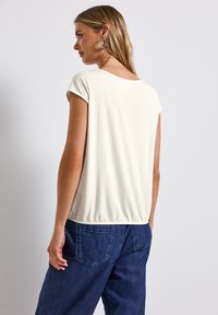 Haut à manches courtes en crème clair avec une texture douce et un ourlet élastiqué, associé à un pantalon en denim bleu avec des poches arrière.