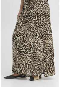 Robe maxi imprimé léopard en tissu beige et noir; présente une coupe ample avec des fentes sur les côtés et des chaussures à bout pointu noires et crème.