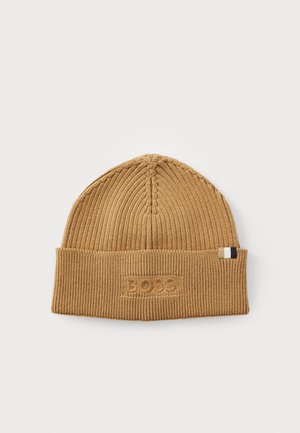 Knit beanie in a light brown color with ribbed texture, featuring an embroidered logo and a small striped accent on the side.
