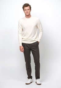 Maglione crema, pantaloni scuri e sneakers bianche. Il maglione ha maniche lunghe e un collo rotondo. I pantaloni sono su misura con un tessuto testurizzato.