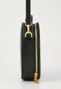 Rund svart läderväska med texturerad yta, med guldfärgad dragkedja och detaljer, samt ett avtagbart bärhandtag.