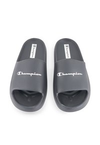 Sandali in gomma nera con design open toe, caratterizzati da una fascia larga e la scritta "Champion" in lettere bianche sulla parte anteriore.