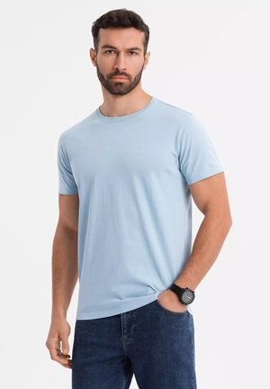 Camiseta de manga corta azul claro en un corte relajado, hecha de algodón con una textura suave. Llevada con jeans azul oscuro y un reloj negro.
