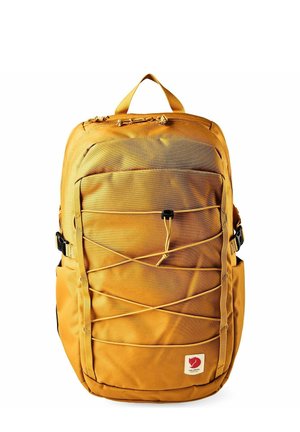 Zaino giallo senape con cordino elastico frontale, tasche laterali, manico superiore, chiusura con cerniera e piccolo logo di volpe rossa in basso a destra.