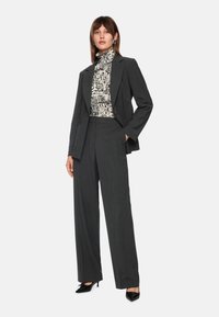 Gray tailored suit with a long blazer and wide-leg trousers, paired with a black and white patterned turtleneck and black high heels.