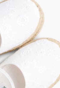 Espadrilles de tela blanca con bordado floral, suelas de yute natural y diseño de punta redonda. Superficie texturizada con ligero brillo.