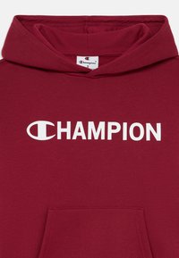Felpa con cappuccio color bordeaux, dotata di tasca frontale e grande logo bianco "CHAMPION". Realizzata in tessuto morbido con una texture liscia.
