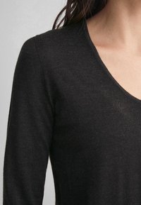 Haut noir à manches longues en tissu tricoté doux. Présente un décolleté en V et épouse le corps avec une texture lisse.