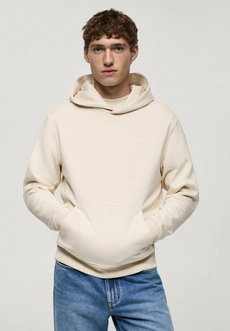 Crème-kleurige hoodie gemaakt van zachte stof, met een kangoeroezak, geribbelde boorden en een losse pasvorm. Gecombineerd met blauwe jeans.