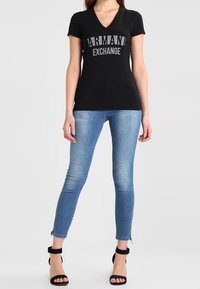 Czarny t-shirt z dekoltem w serek z srebrnym napisem logo, w połączeniu z jasnoniebieskimi rurkami i czarnymi sandałkami na kostkę. Prosty design i krój.