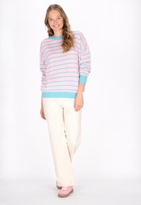 Lichtroze sweater met turquoise strepen, ronde halslijn, geribde manchetten, gecombineerd met crèmekleurige wijde broek en roze sneakers.