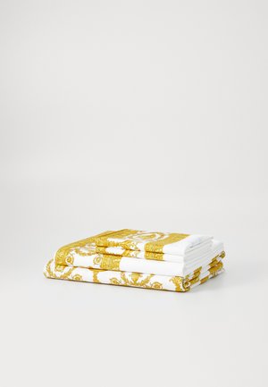 Toallas de algodón dobladas con tela blanca y patrones dorados intrincados en los bordes, que presentan detalles ornamentales y un diseño elegante.