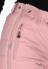 Roze geïsoleerde broek met een rits aan de voorkant en zijzakken, een elastische tailleband en een klein Zweeds vlagdetail aan de zijkant.