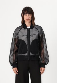 Black bomber jacket made of mesh material, featuring a zip closure, ribbed cuffs, and embroidered logo across the chest.