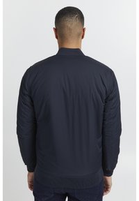 Giacca bomber color navy con una finitura liscia e leggera, polsini e orlo a costine, con texture trapuntata sulle maniche e sulla schiena.