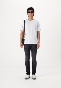 Witte T-shirt, zwarte jeans, zwarte zonnebril en zwarte schoudertas. Schoeisel heeft een wit en grijs ontwerp met zwarte accenten.