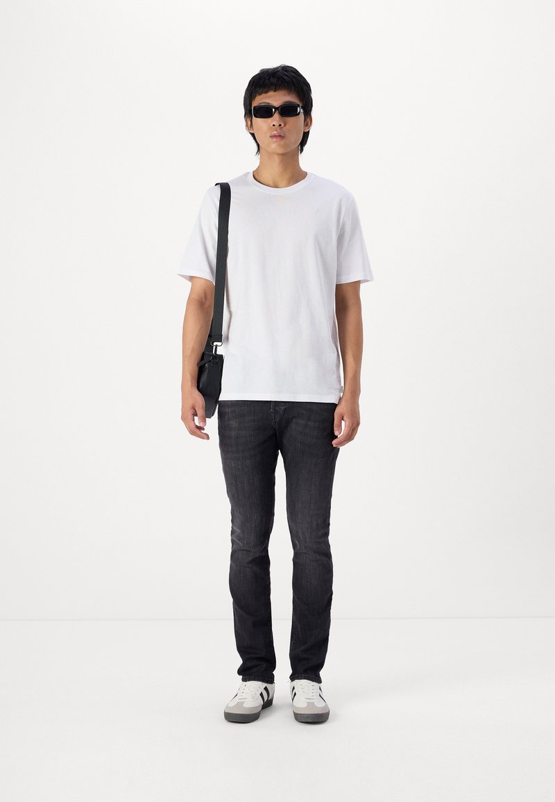 Witte T-shirt, zwarte jeans, zwarte zonnebril en zwarte schoudertas. Schoeisel heeft een wit en grijs ontwerp met zwarte accenten.