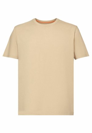 T-shirt beige en coton à manches courtes, col rond, et coupe décontractée. Porté avec un jean denim bleu, mettant en avant un look casual.