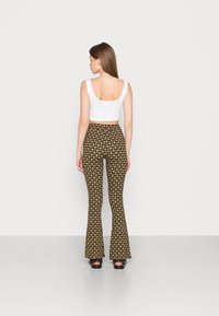 Calças flare de cintura alta com uma base castanha e um padrão repetido em amarelo e branco, combinadas com um top cropped branco. Textura suave.