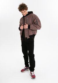 Herrarnas bomberjacka i mauve, med dragkedja fram, sidofickor med dragkedja och ribbade muddkanter. Kombinerad med svarta cargobyxor och flerfärgade sneakers.