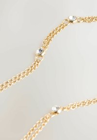 Gold chain bracelet featuring multiple links, adorned with shiny round clear crystals at intervals, showcasing a delicate design and smooth texture.