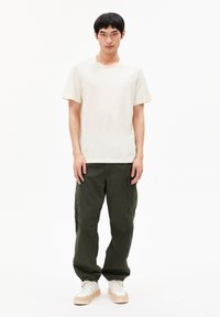 Weißes Baumwoll-T-Shirt mit Rundhalsausschnitt, kombiniert mit dunkelgrünen Cargo-Hosen mit Seitentaschen und elastischen Bündchen, getragen mit weißen Sneakers.