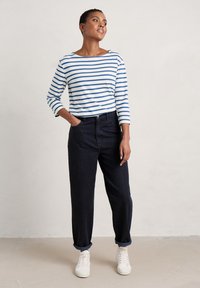 Camisa de manga larga a rayas en blanco y azul, combinada con pantalones vaqueros oscuros y zapatillas blancas. Estilo casual, con los puños de los pantalones enrollados.